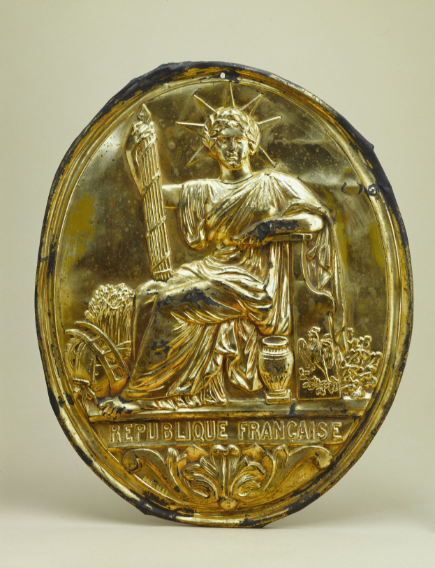 Goldenes rundes Schild mit einer Reliefdarstellung der Freiheitsstatue und eingraviertem Text auf einem weißen Hintergrund.