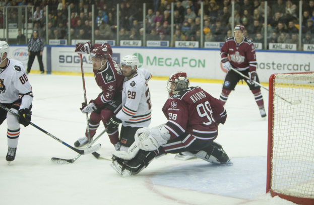Gruppe von Menschen, die Hockey auf einem Eisstadion spielen, mit Tor auf der rechten Seite, tragen Helme und halten Stöcke, Zuschauer in Tribüne mit Bannern im Hintergrund.