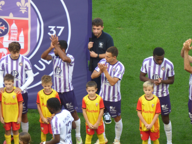 Eine Gruppe junger Jungs auf einem Fußballfeld stehend, die klatschen, mit einem Banner mit Text und Logos im Hintergrund.