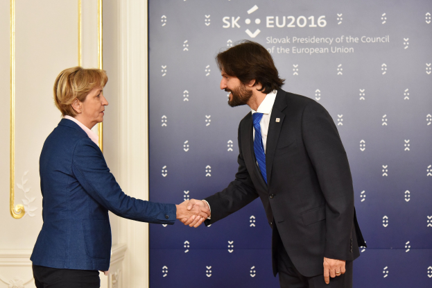 Bundeskanzlerin Angela Merkel und Bundeskanzler Joachim Gauck geben sich die Hand vor einem Banner mit der Aufschrift 'EU-Gipfel', während sie freundlich und einladend lächeln.