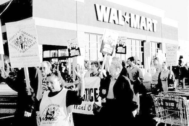 Schwarz-weißes Bild von Menschen, die vor einem Einkaufszentrum protestieren und Plakate halten.