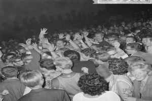 Ein Schwarz-Weiß-Bild einer Menge auf einem Konzert mit erhobenen Händen um eine Tafel herum.