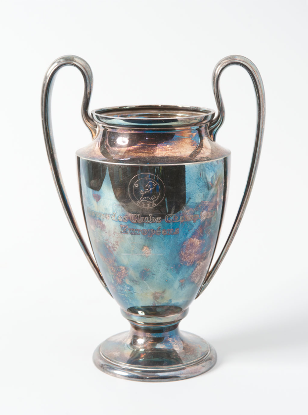Der UEFA-Champions-League-Pokal, ein stählerner Pokal mit zwei Griffen und einem blauen und silbernen Farbschema, der mit "UEFA Champions League" beschriftet ist, vor einem weißen Hintergrund.