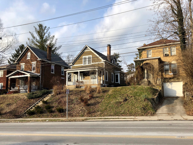 Reihe von Häusern mit Fenstern, Türen, Säulen, Geländern, Stufen, Pflanzen und einem Pfahl mit einer Tafel, die gegen einen bewölkten Himmel gesetzt ist, repräsentiert eines der teuersten Häuser zum Verkauf in Detroit.